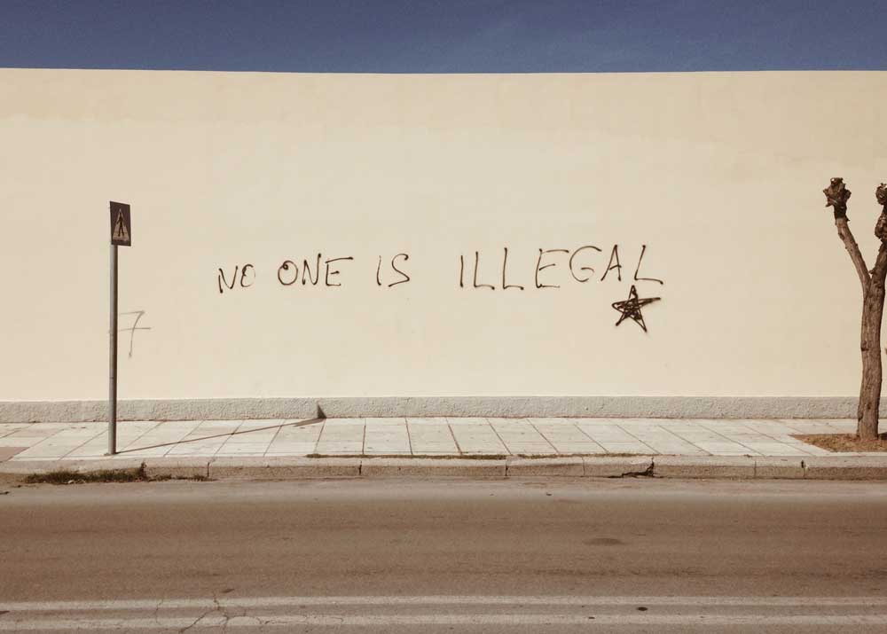 Image of a mural on an outside wall that says "no one is illegal."